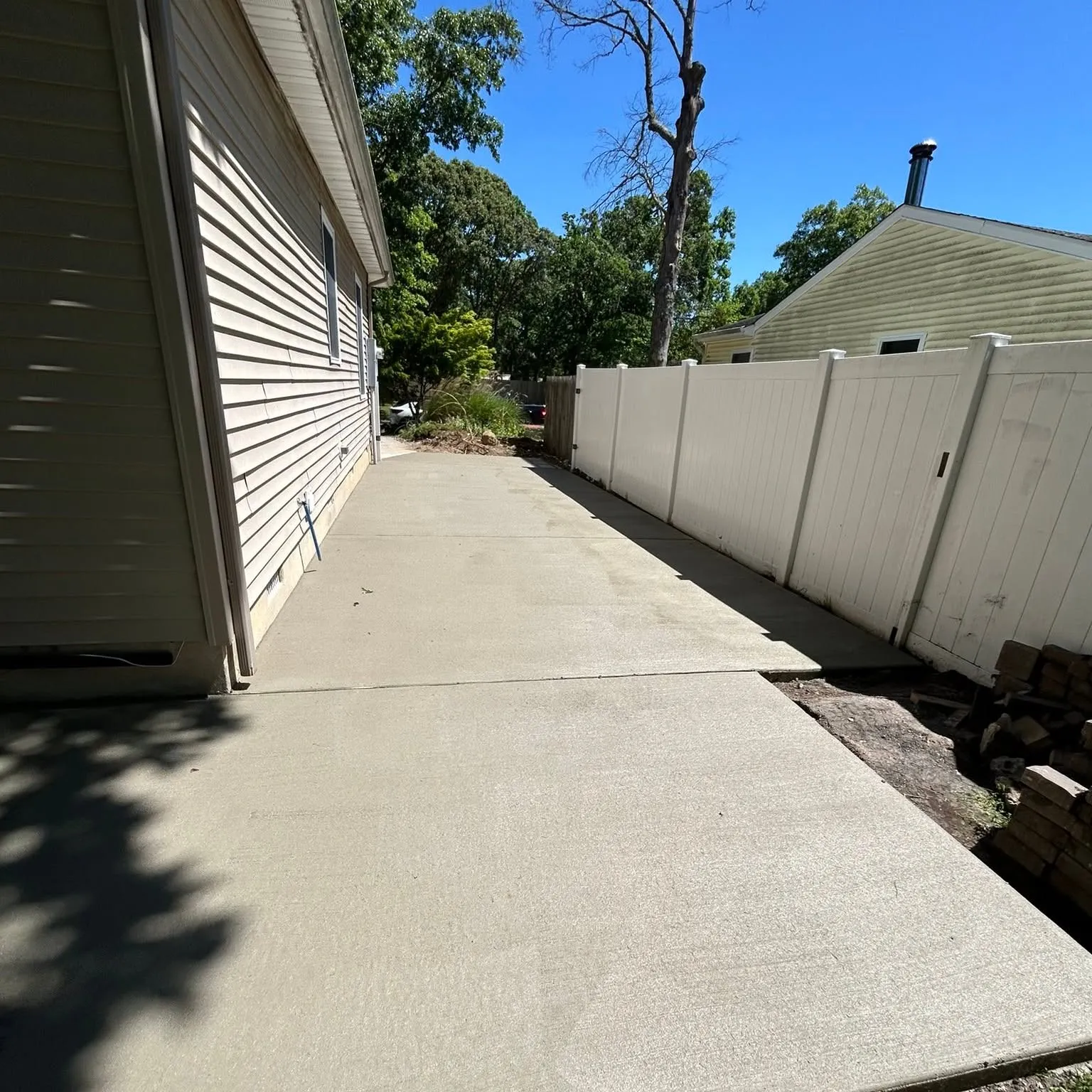 Poured concrete walkway running down a side yard between a home and vinyl fence in South Jersey